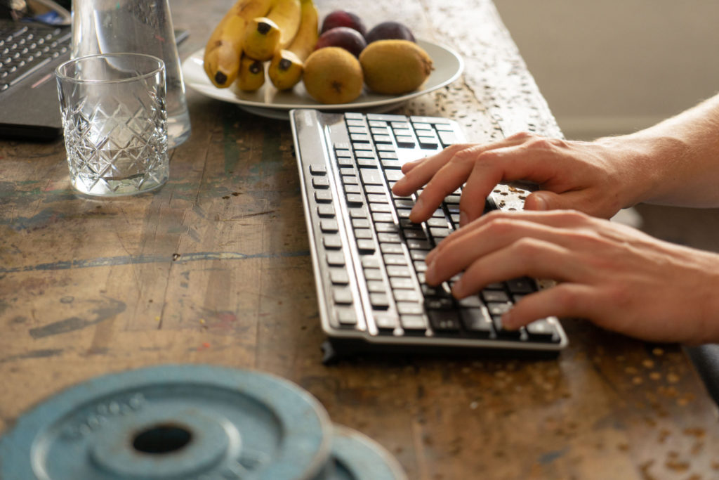 Mann tippt umgeben von gewichten und Obst auf einer Tastatur